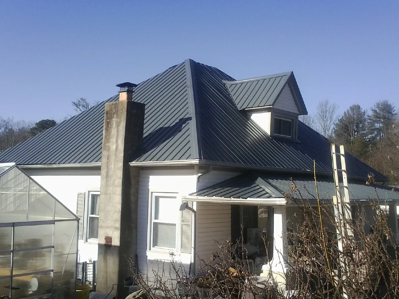 Dark blue standing seam metal roof on a white farmhouse with dormer — Slate & Tile Roof Repair by Roofing Brothers in Millersville