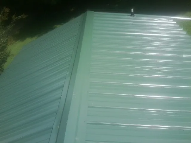 New green metal panels meeting at the ridge of a roof — Flat Roof Repair work by our crew in Millersville